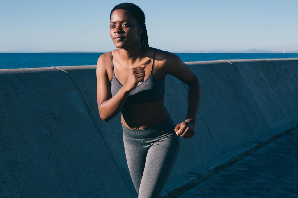 Healthy woman jogging along the oceanfront on a sunny day, embodying fitness and vitality.