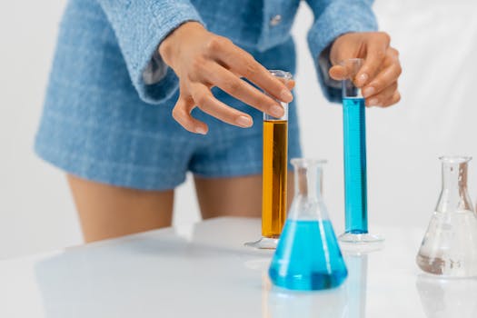 Hands arranging colorful liquids in laboratory glassware for a science experiment.